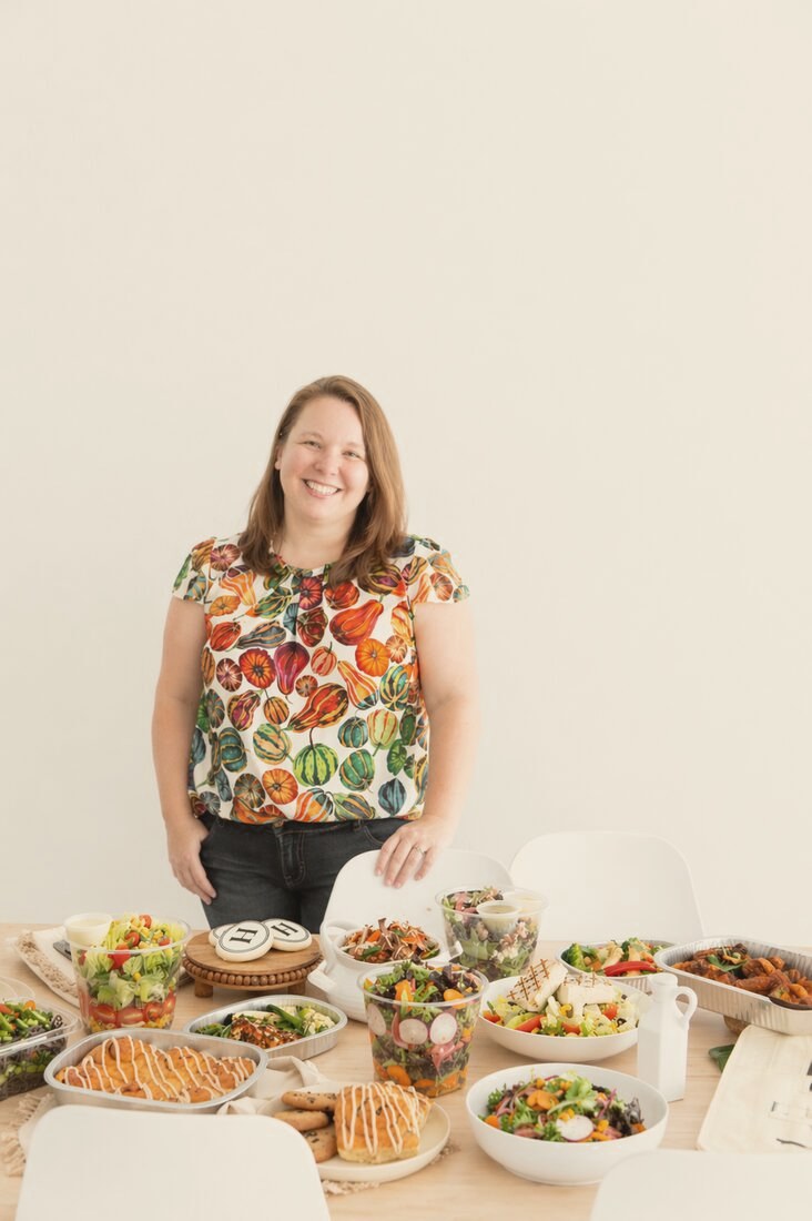 Rosie Gizelt, founder of Click to Table, behind a spread of catered salads, boxed meals, and appetizers
